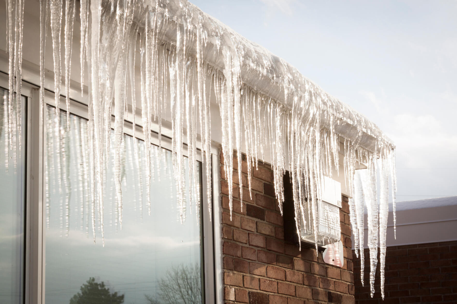 Preventing Ice Dams. Image of a house's gutters filled with an ice dam causing large icicles to hang from the edge of the roof.