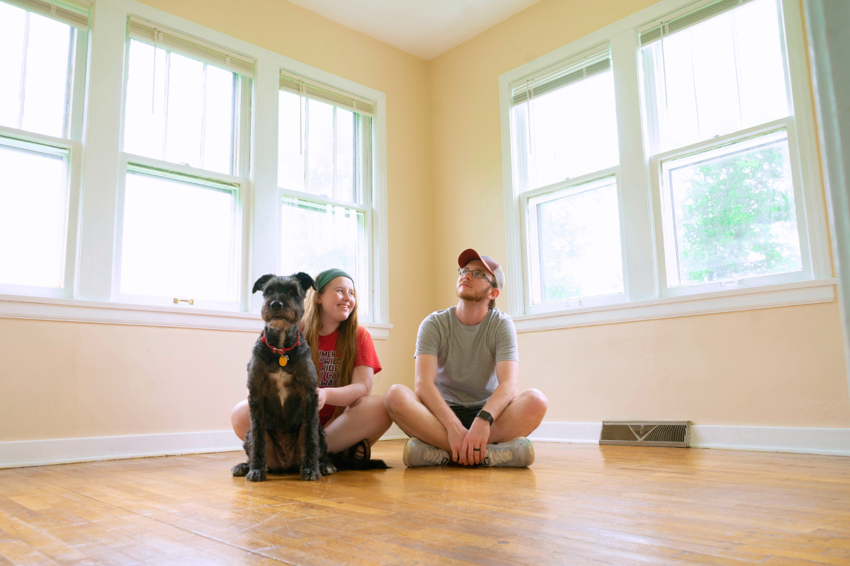 Navigating Roof Care as a First Time Homeowner. Image of a couple and their dog sitting on the floor of an empty room in their new home.